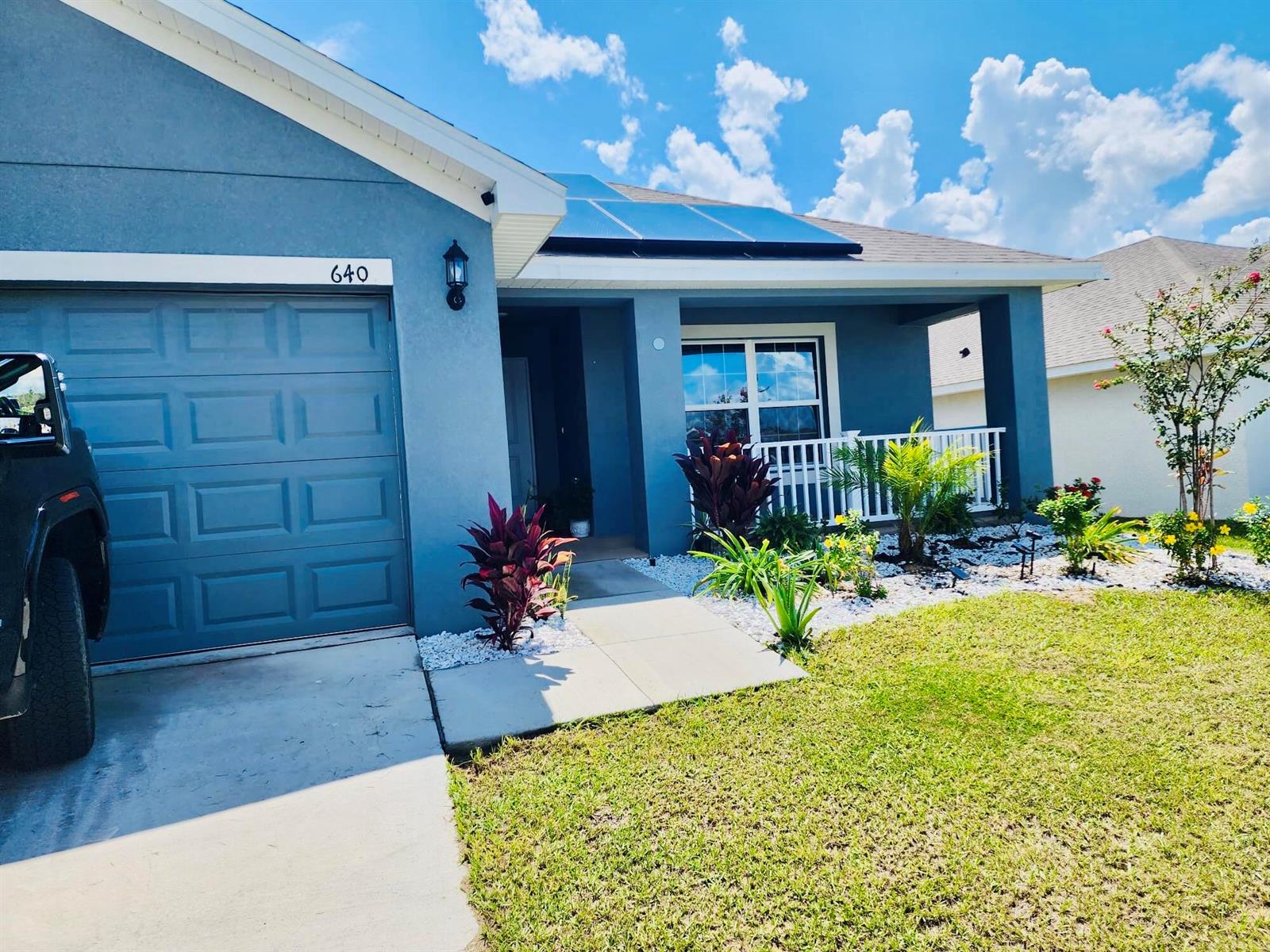 The exterior of a blue single-story house features a garage, solar panels, and landscaping — 640 Tanaro Lane, FL 33844, FL