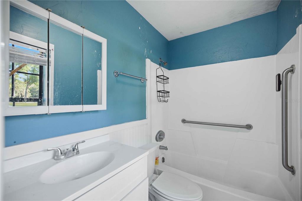 A bathroom features a white vanity, a toilet, and a shower-tub combo with grab bars — 2351 NE 40TH STREET, OCALA, FL