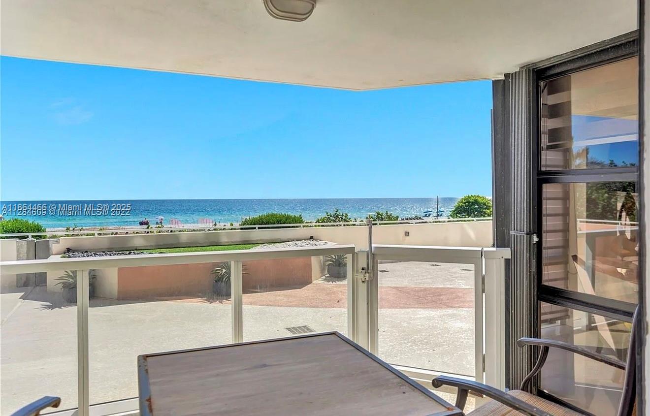 A balcony with a table and chairs overlooks a beach and the ocean — 6423 E Collins Ave # 206, Miami Beach FL 33141, MIAMI BEACH, FL