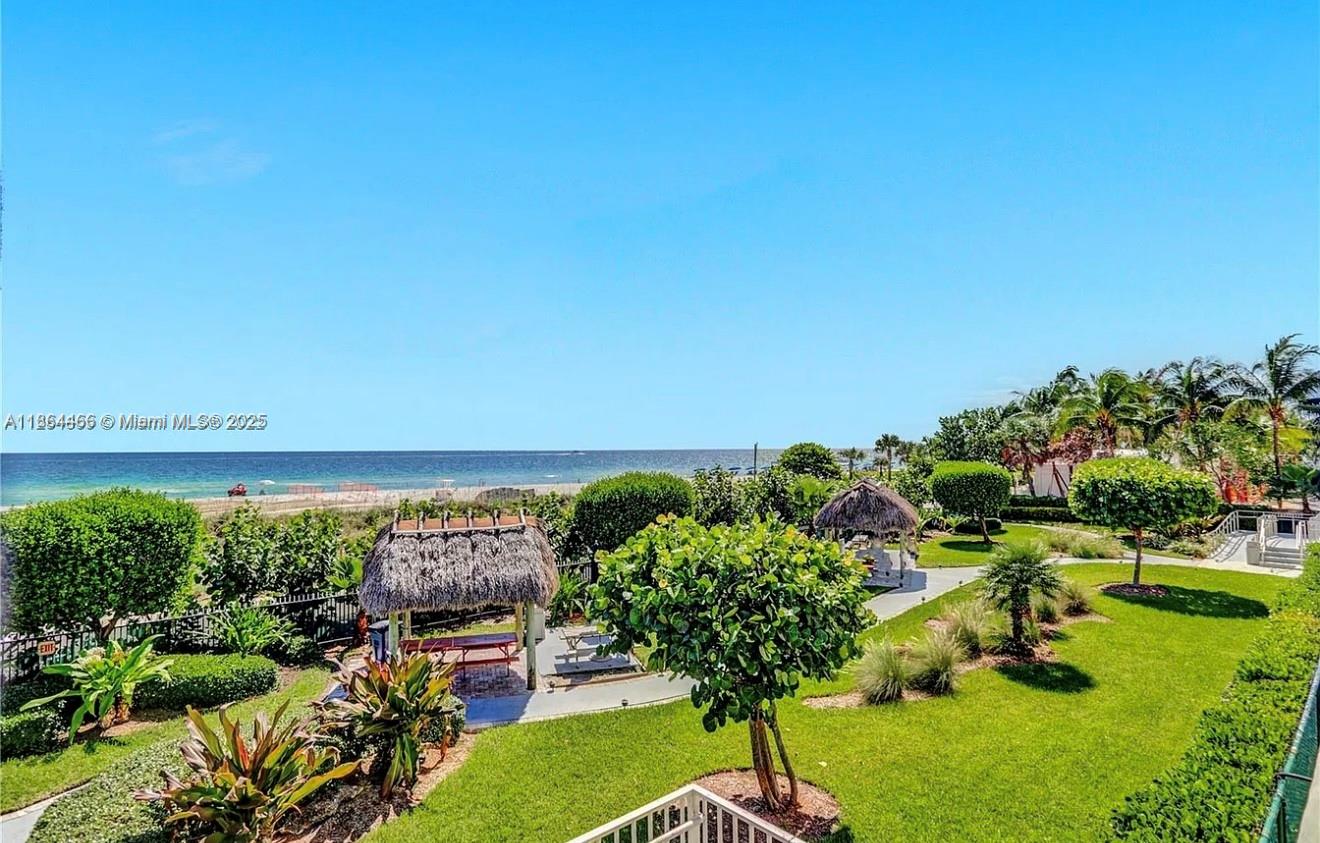 An elevated view of a grassy courtyard with tiki huts overlooking a sandy beach and ocean — 6423 E Collins Ave # 206, Miami Beach FL 33141, MIAMI BEACH, FL