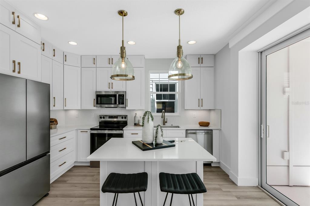 A modern kitchen features white cabinetry, stainless steel appliances, a center island, and pendant lighting — 2138 W CHESTNUT STREET, TAMPA, FL