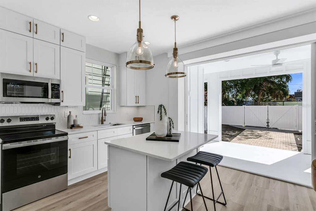 A modern white kitchen features a center island, stainless steel appliances, and an open patio — 2138 W CHESTNUT STREET, TAMPA, FL