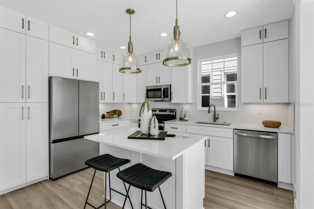 A modern kitchen features white cabinetry, stainless steel appliances, a center island, and wood flooring — 2138 W CHESTNUT STREET, TAMPA, FL