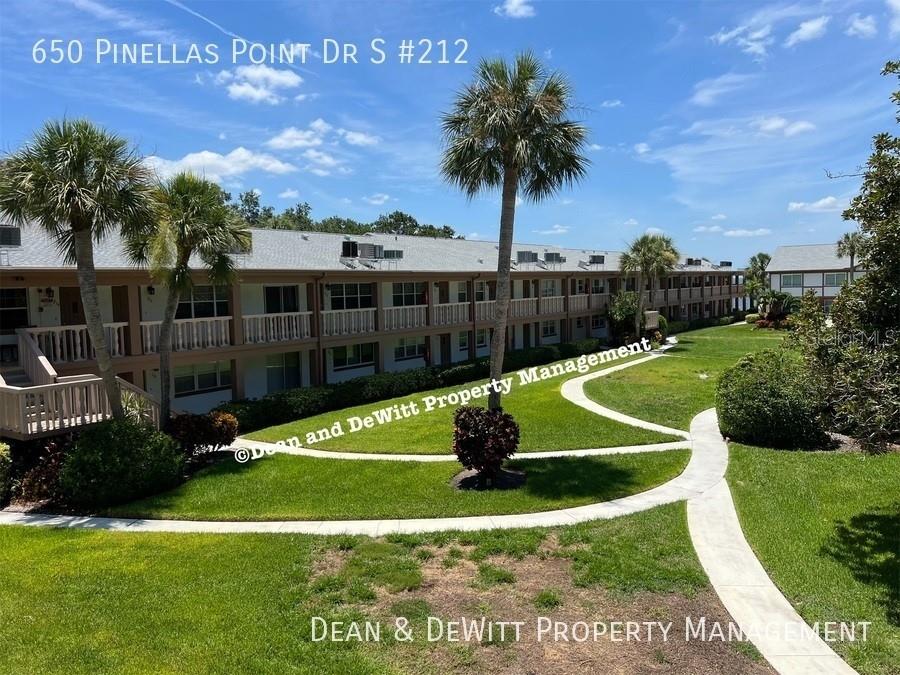 A multi-story apartment building features balconies overlooking a landscaped courtyard with palm trees and walkways — 650 PINELLAS POINT DRIVE S UNIT 212, ST PETERSBURG, FL