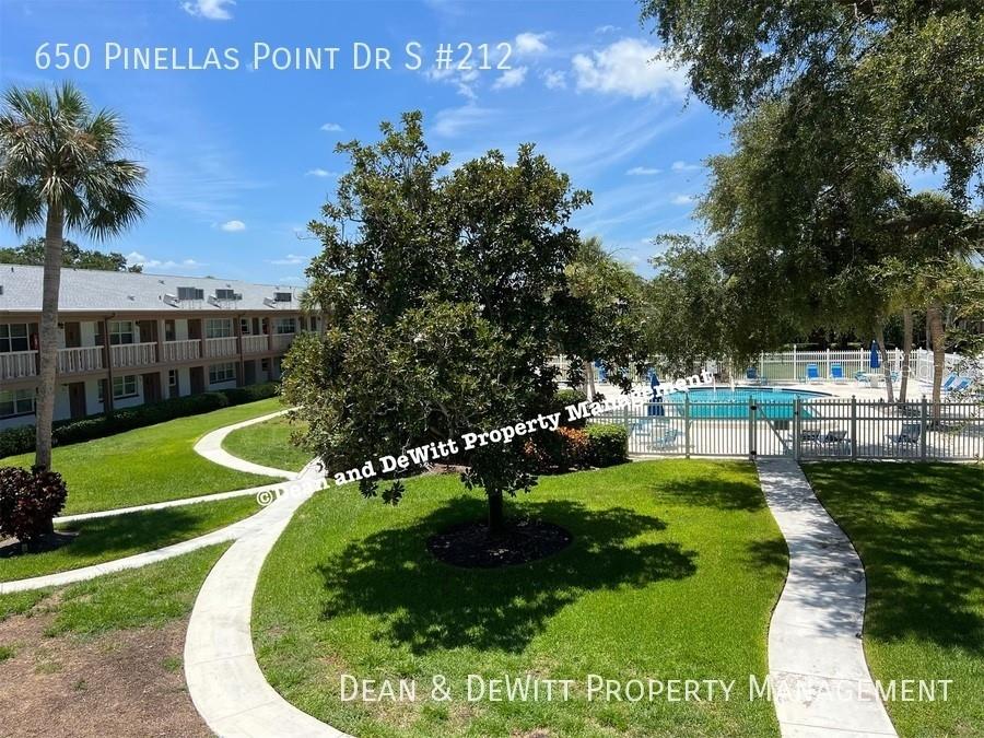 A view of a grassy courtyard with a swimming pool and a multi-story apartment building — 650 PINELLAS POINT DRIVE S UNIT 212, ST PETERSBURG, FL