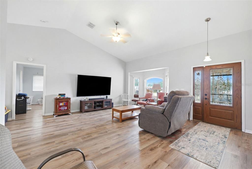 A living room features vaulted ceilings, wood-look flooring, a wall-mounted television, and a front entryway — 10154 SPRING HILL DRIVE, SPRING HILL, FL