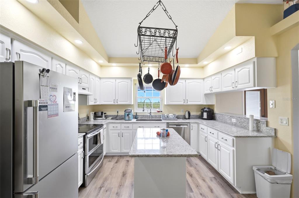 A kitchen features white cabinets, granite countertops, stainless steel appliances, and a hanging pot rack — 10154 SPRING HILL DRIVE, SPRING HILL, FL