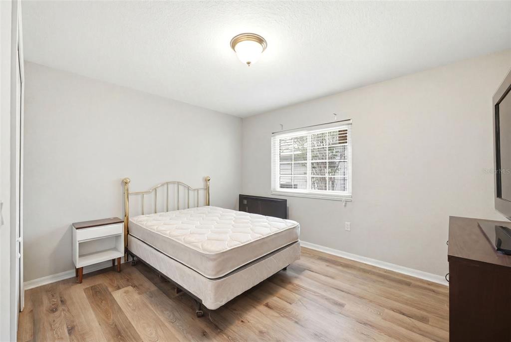 A bedroom with light wood-look flooring, a brass bed frame, and a window with blinds — 10154 SPRING HILL DRIVE, SPRING HILL, FL