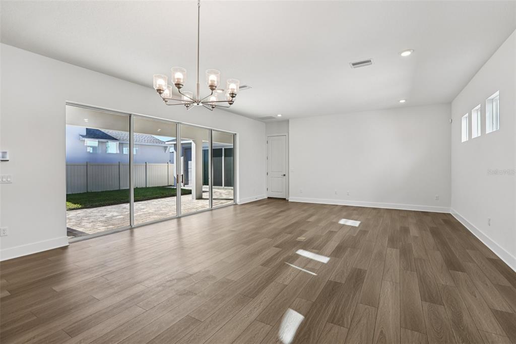 An empty living room features wood-look flooring, a modern chandelier, and large sliding glass doors — 10707 TORCHWOOD SEA WAY, SAN ANTONIO, FL