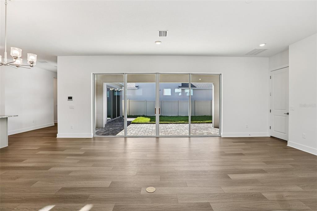 A living room with light wood-look flooring and large sliding glass doors leading to a patio — 10707 TORCHWOOD SEA WAY, SAN ANTONIO, FL