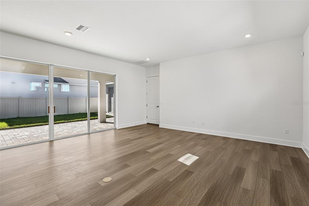 An empty room features wood-look flooring, white walls, recessed lighting, and sliding glass patio doors — 10707 TORCHWOOD SEA WAY, SAN ANTONIO, FL