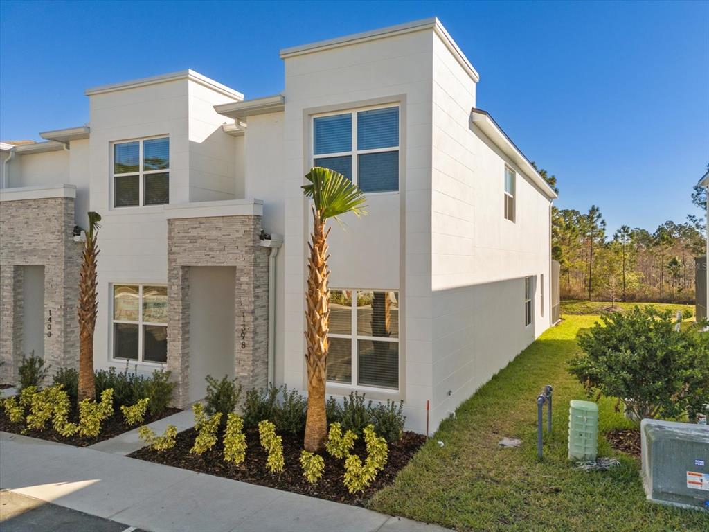 A two-story white townhouse with stone accents, palm trees, and a small front yard — 1398 PEACEFUL NATURE WAY, CLERMONT, FL