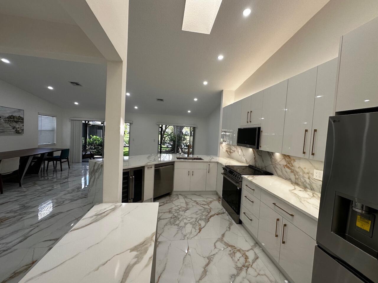 A modern kitchen features white glossy cabinets, marble-patterned countertops, and matching marble tile flooring — 2173 Discovery Circle W, Deerfield Beach FL 33442, DEERFIELD BEACH, FL