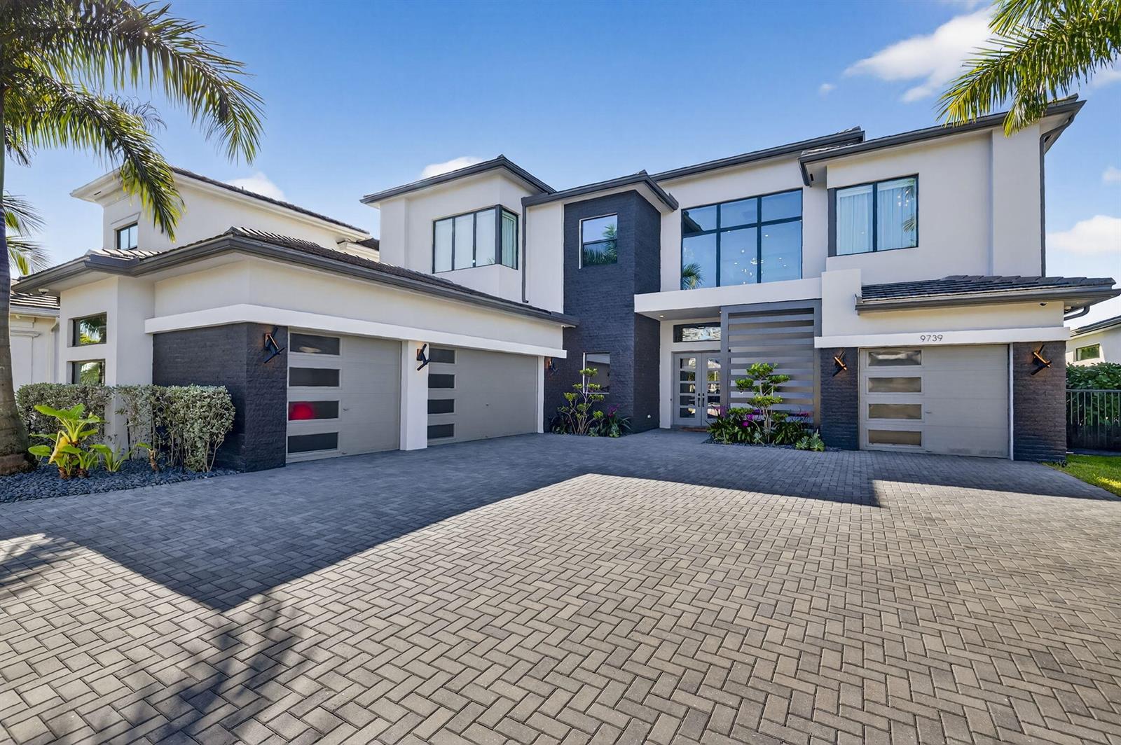 A modern two-story house features a paved driveway, three garage bays, and dark brick accents — 9739 Chianti Classico Terrace, Boca Raton FL 33496, BOCA RATON, FL