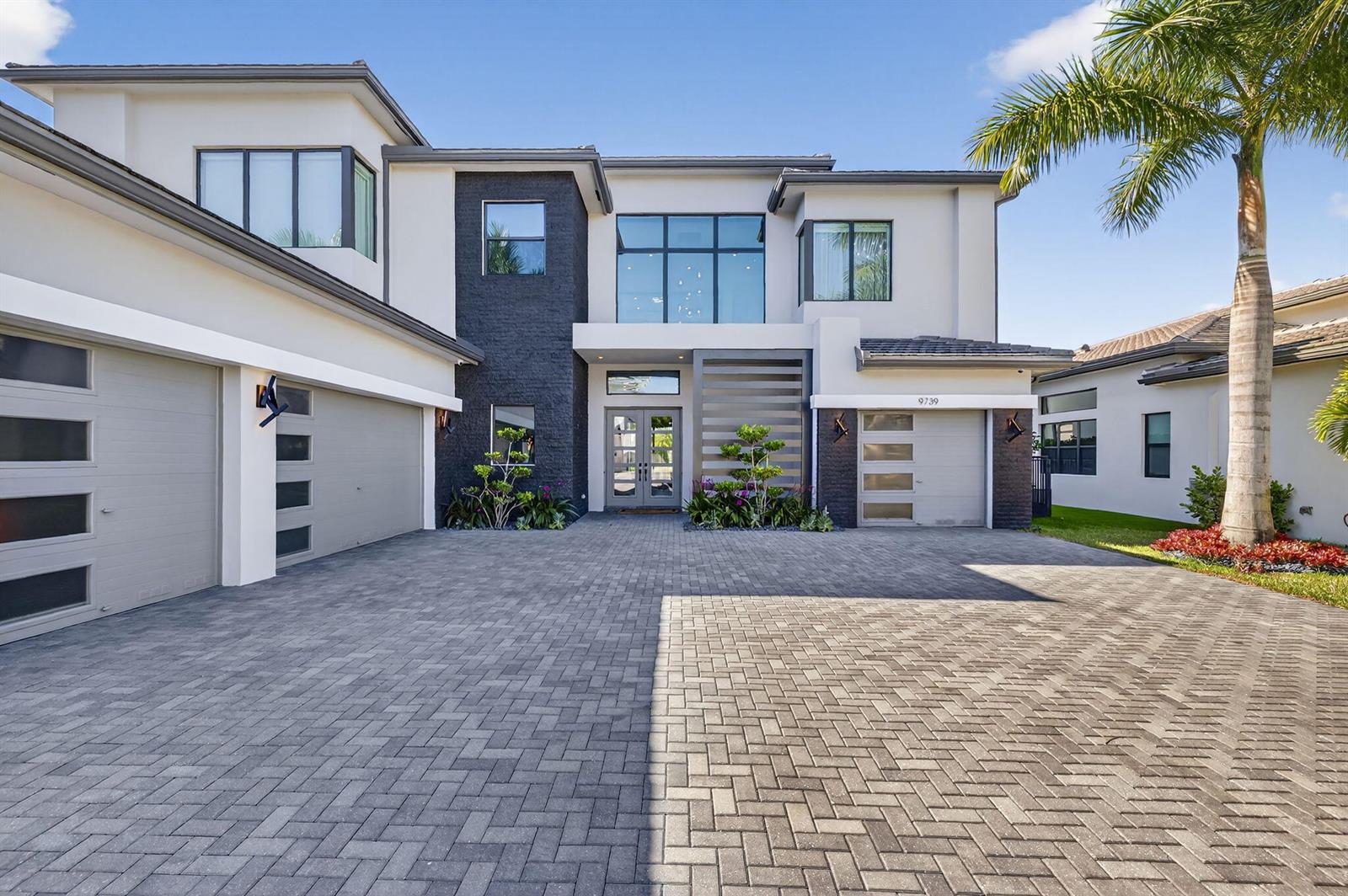 A modern two-story house features a paved driveway, three garage bays, and dark stone accents — 9739 Chianti Classico Terrace, Boca Raton FL 33496, BOCA RATON, FL