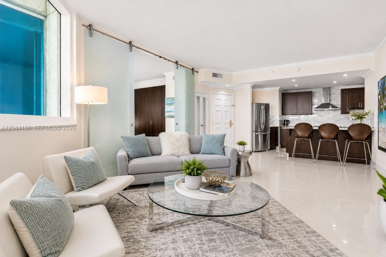 A living room with a glass coffee table, gray sofa, and an open kitchen area — 300 S Pointe Dr # 706, Miami Beach FL 33139, MIAMI BEACH, FL