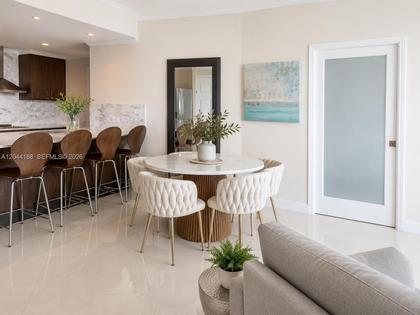 A dining area features a round marble table with tufted chairs near a kitchen island — 300 S Pointe Dr # 706, Miami Beach FL 33139, MIAMI BEACH, FL