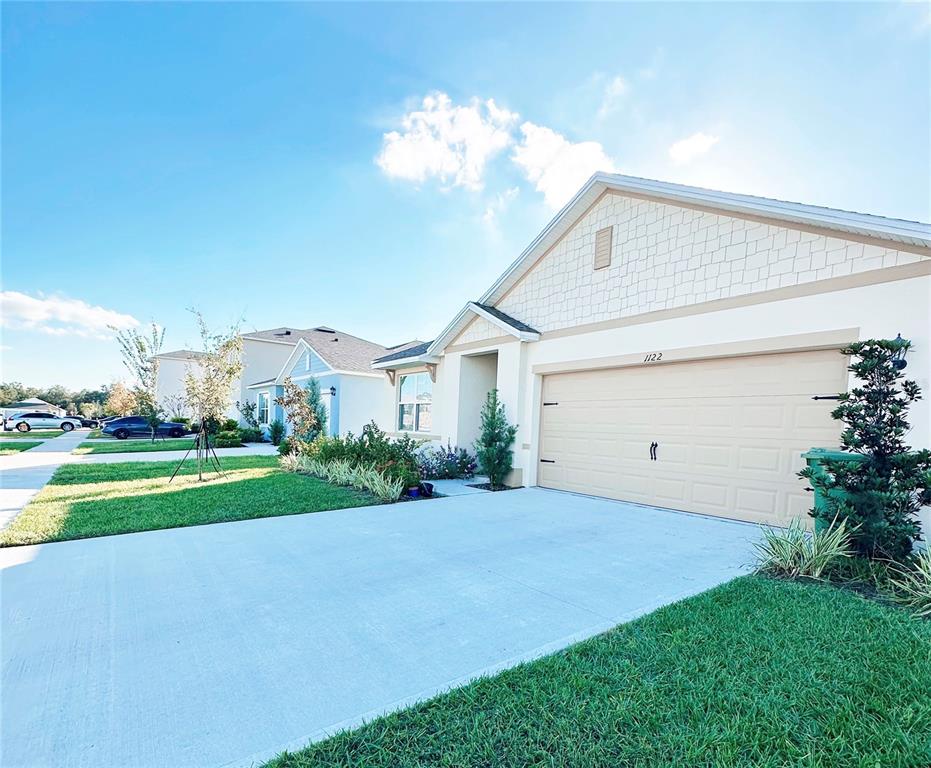 A single-story house with a beige garage and light-colored siding under a blue sky — 1122 BRIMSTONE CIR, WINTER HAVEN, FL
