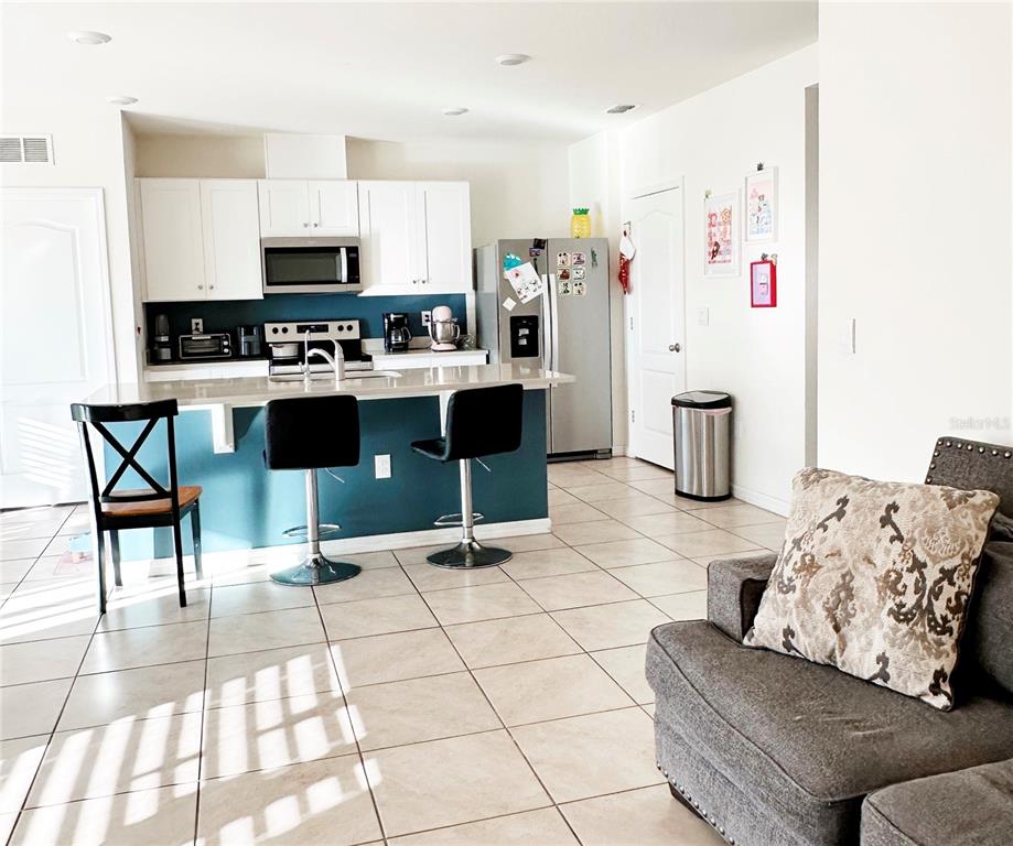 A kitchen with white cabinets, a teal island, and stainless steel appliances opens to a living area — 1122 BRIMSTONE CIR, WINTER HAVEN, FL