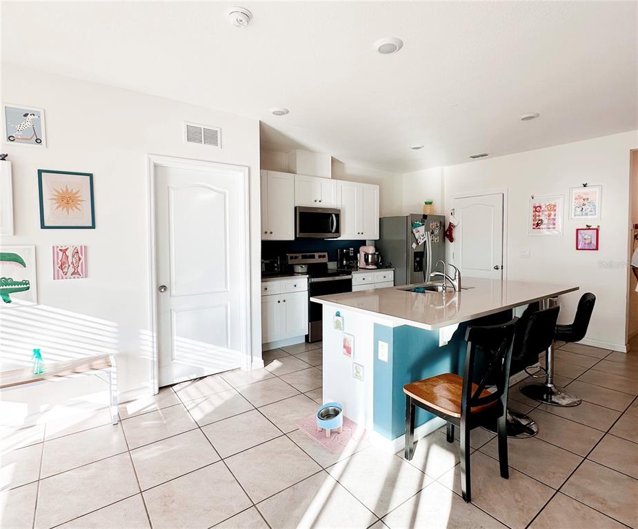 A kitchen features white cabinets, a blue island with bar seating, and light tile flooring — 1122 BRIMSTONE CIR, WINTER HAVEN, FL