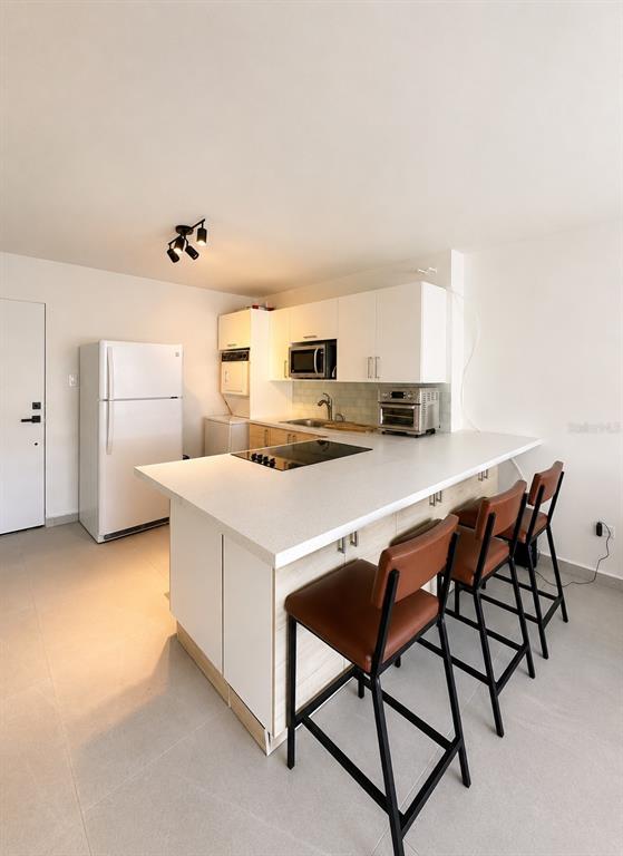 A modern kitchen features white cabinetry, a white island with bar seating, and stainless appliances — 0 C. HORIZONTE, CAROLINA, PR