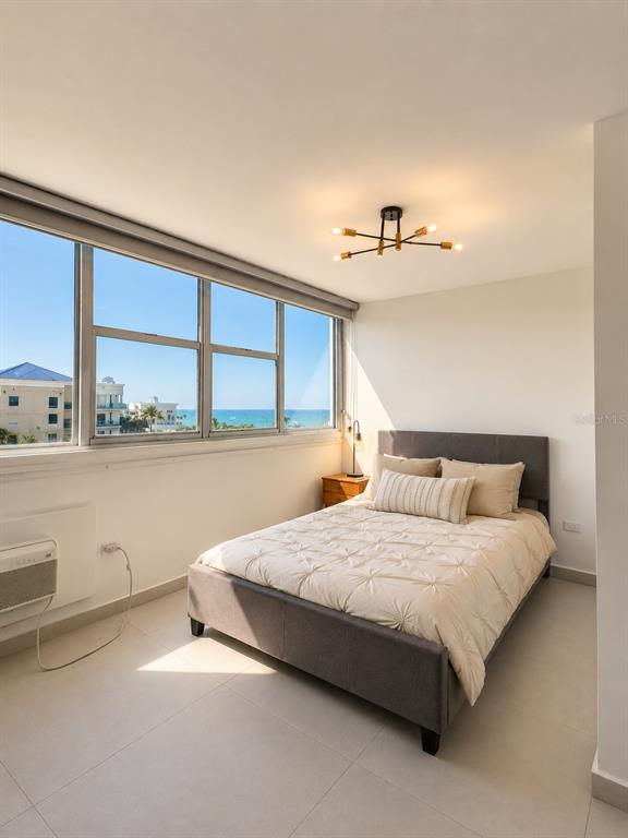 A bedroom features a gray bed, a modern light fixture, and a window overlooking the ocean — 0 C. HORIZONTE, CAROLINA, PR
