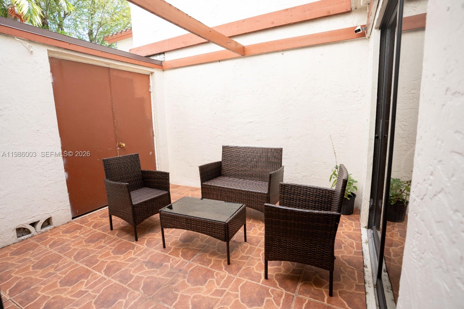 A patio features brown wicker furniture, tiled flooring, and a wooden pergola overhead — 333 Ives Dairy Rd # A33306, Miami FL 33179, MIAMI, FL