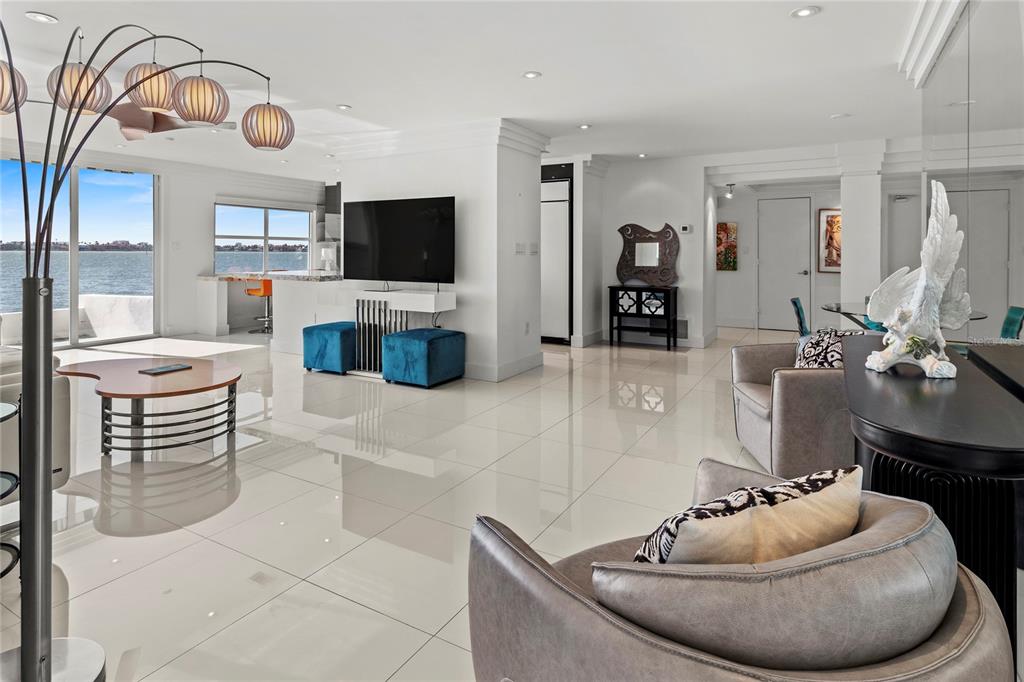 A bright, open-concept living room features white tile floors, a waterfront view, and modern furniture — 400 GOLDEN GATE POINT UNIT 11, SARASOTA, FL