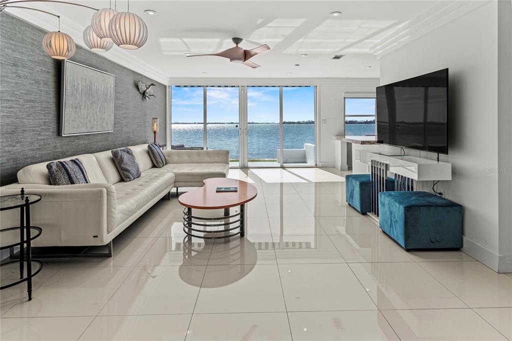 A modern living room features a white sectional sofa, tile floors, and large waterfront windows — 400 GOLDEN GATE POINT UNIT 11, SARASOTA, FL