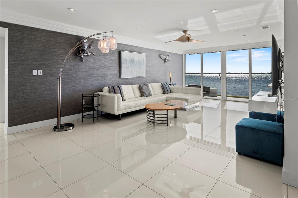 A modern living room features a white sectional sofa, gray textured wall, and waterfront views — 400 GOLDEN GATE POINT UNIT 11, SARASOTA, FL