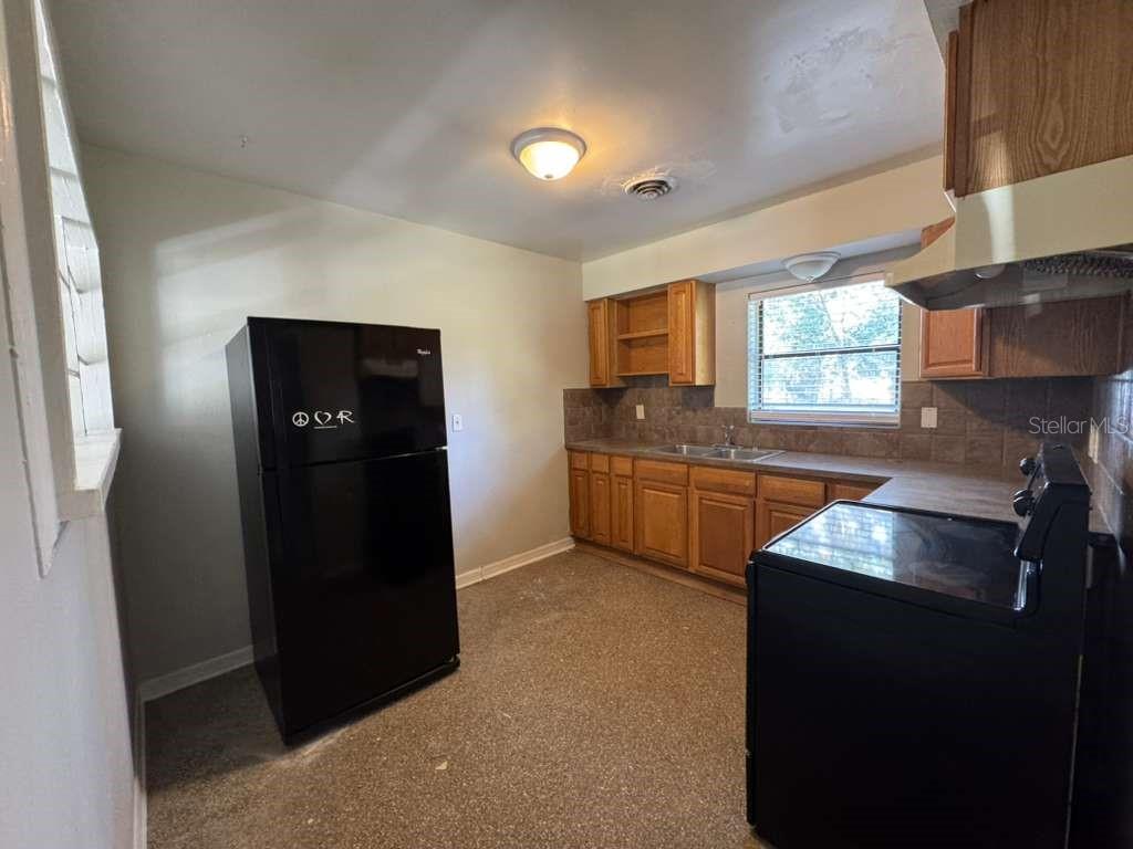 A kitchen features wood cabinets, dark countertops, black appliances, and a window above the sink — 5717 FERNHILL DRIVE, ORLANDO, FL