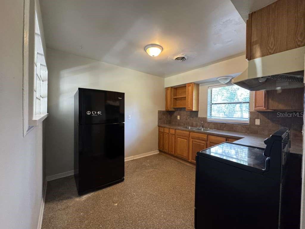 A kitchen features wood cabinets, a black refrigerator, a black stove, and a window — 5717 FERNHILL DRIVE, ORLANDO, FL