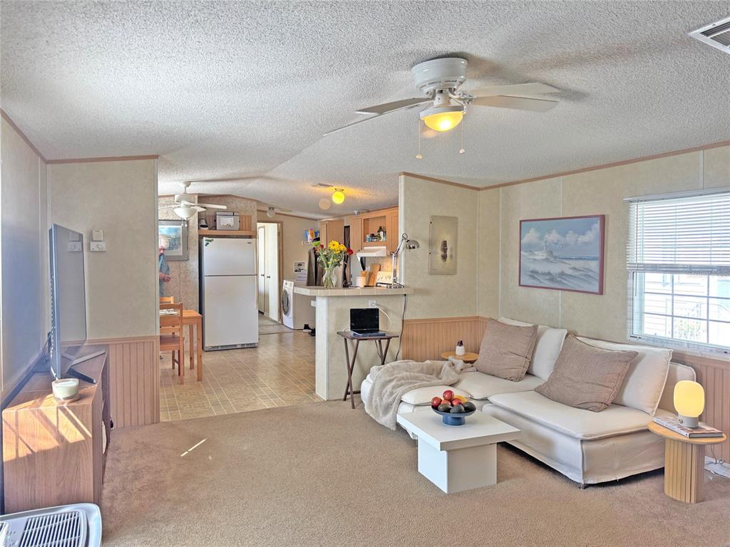 A living room with beige carpet and walls flows into a kitchen with light wood cabinets — 10101 BURNT STORE ROAD UNIT 118, PUNTA GORDA, FL