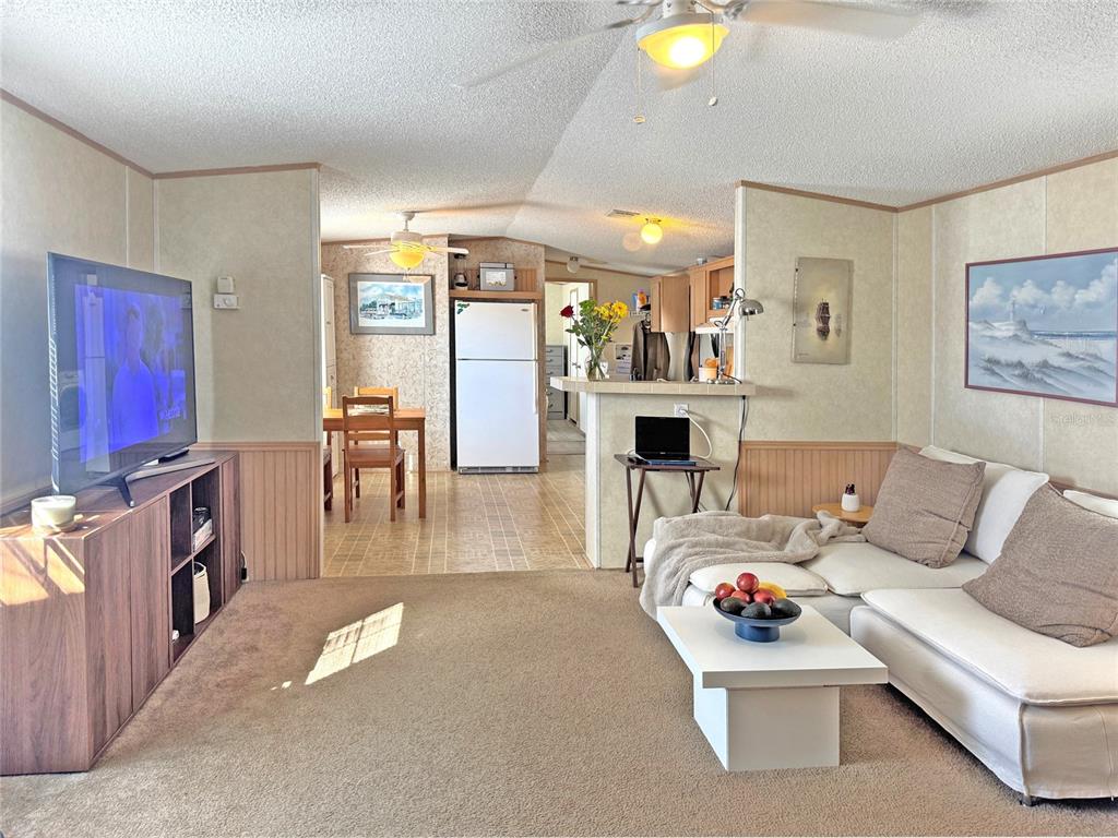 A living room with beige carpet, a white sectional sofa, and an open kitchen area — 10101 BURNT STORE ROAD UNIT 118, PUNTA GORDA, FL
