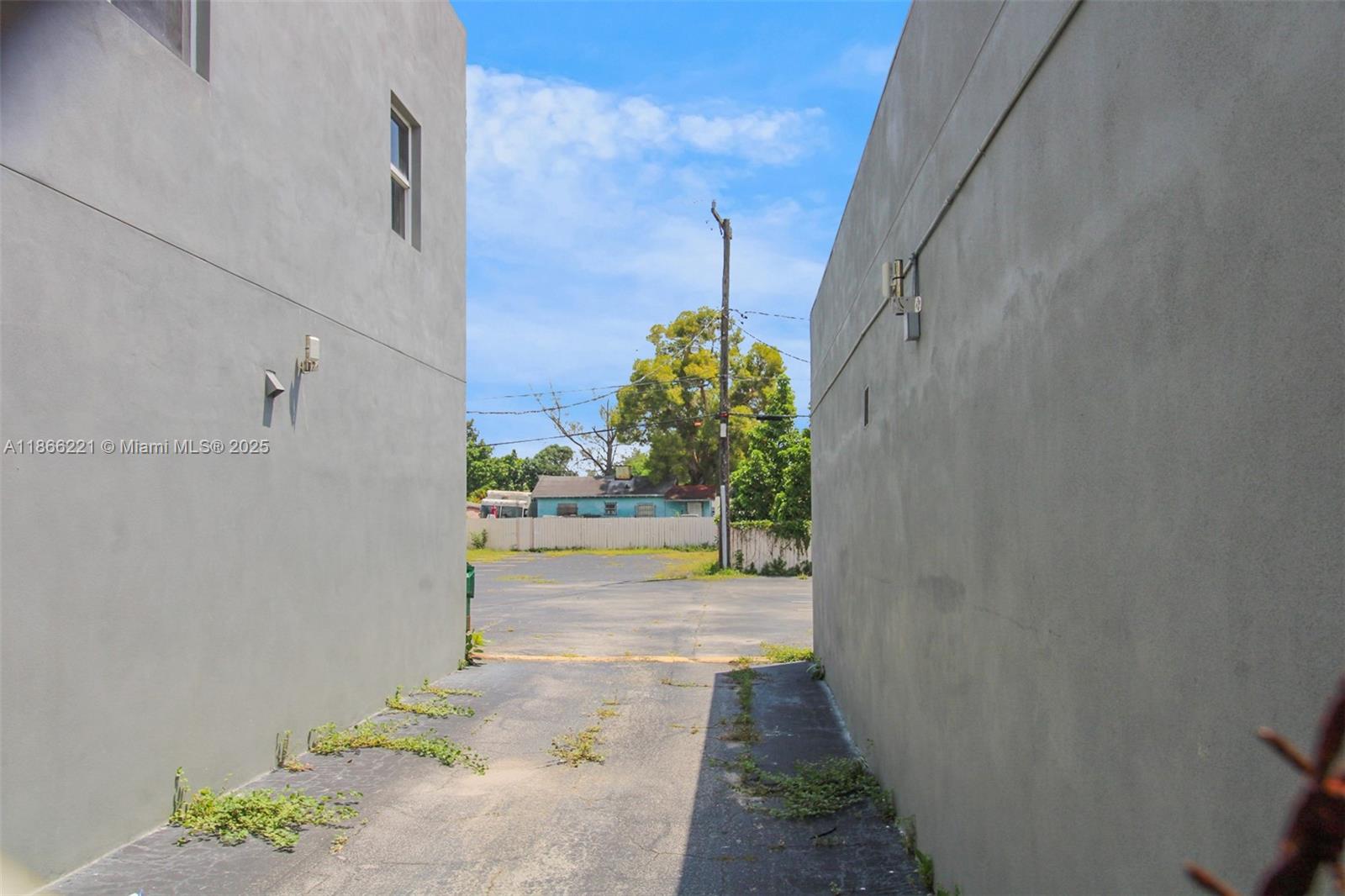 A narrow paved alleyway sits between two plain gray concrete walls leading to a lot — 3267 NW 35th St, Miami FL 33142, MIAMI, FL
