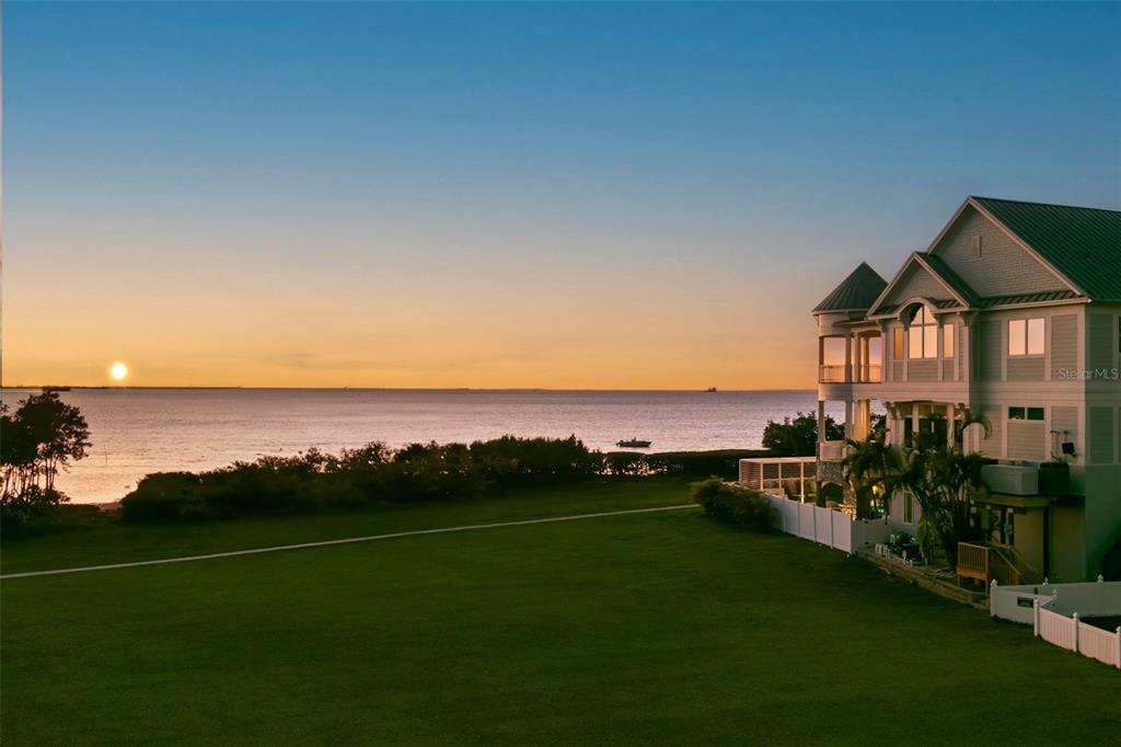 A large multi-story house sits beside a grassy lawn overlooking the ocean at sunset — 606 INDIANA AVENUE, CRYSTAL BEACH, FL