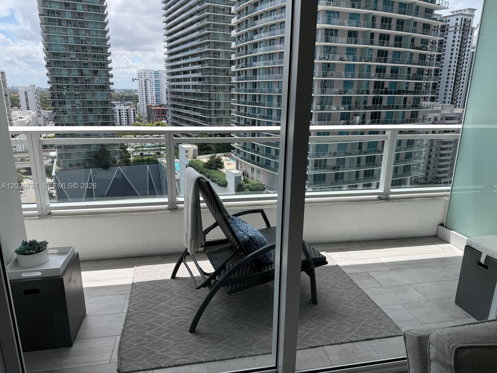 A balcony with a lounge chair, rug, and potted plant overlooks a city skyline — 1080 Brickell Ave # 1703, Miami FL 33131, MIAMI, FL