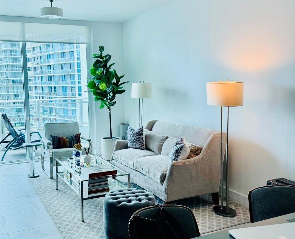 A modern living room features a light-colored sofa, glass coffee table, and a large potted plant — 1080 Brickell Ave # 1703, Miami FL 33131, MIAMI, FL