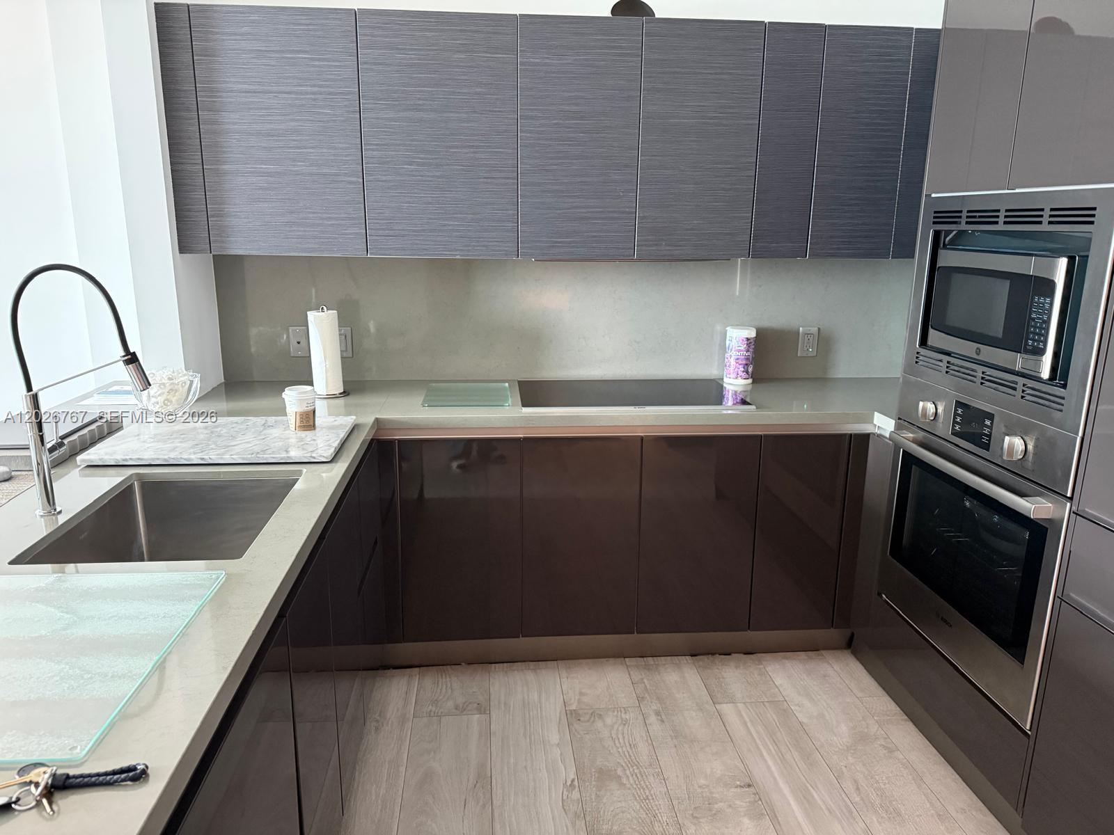 A modern kitchen features dark glossy lower cabinets, textured upper cabinets, and stainless steel appliances — 1080 Brickell Ave # 1703, Miami FL 33131, MIAMI, FL
