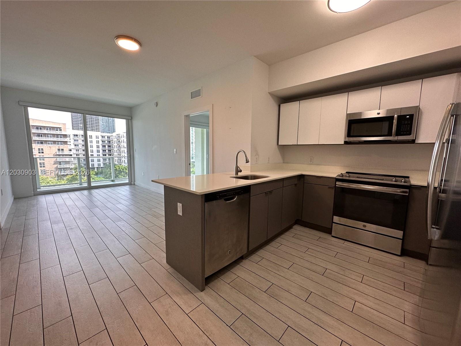 A modern kitchen with stainless steel appliances and white cabinets opens to a living area — 321 NE 26th St # 601, Miami FL 33137, MIAMI, FL