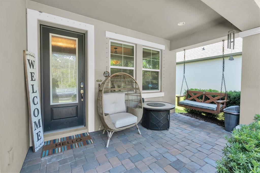 A covered front porch features a paved floor, a hanging bench, and a wicker chair — 3794 NIGHT STAR TRAIL, ODESSA, FL