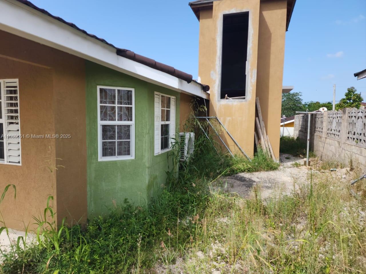 The exterior of a house features tan and green walls, a tower structure, and overgrown landscaping — 00 Stonebrook Vista, Trelawny, NA, NA