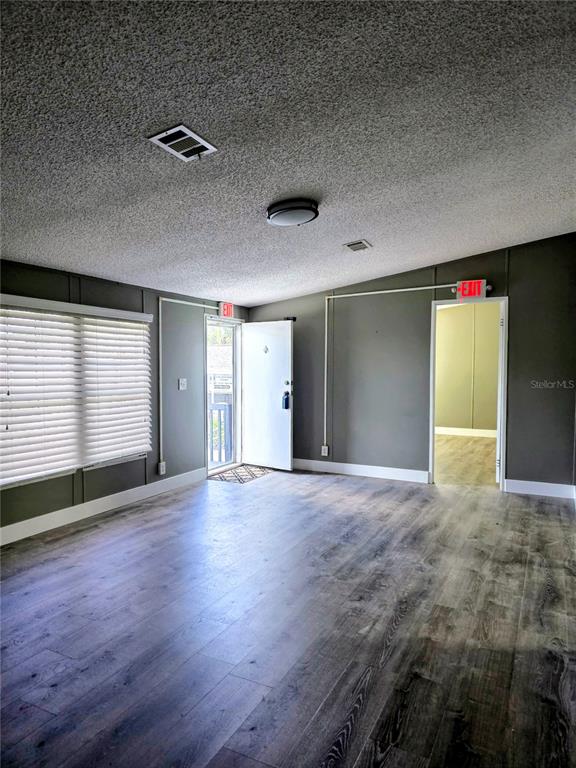 A living room features gray walls, wood-look flooring, a popcorn ceiling, and two exit signs — 205 W SHELL POINT ROAD Bldg A, RUSKIN, FL