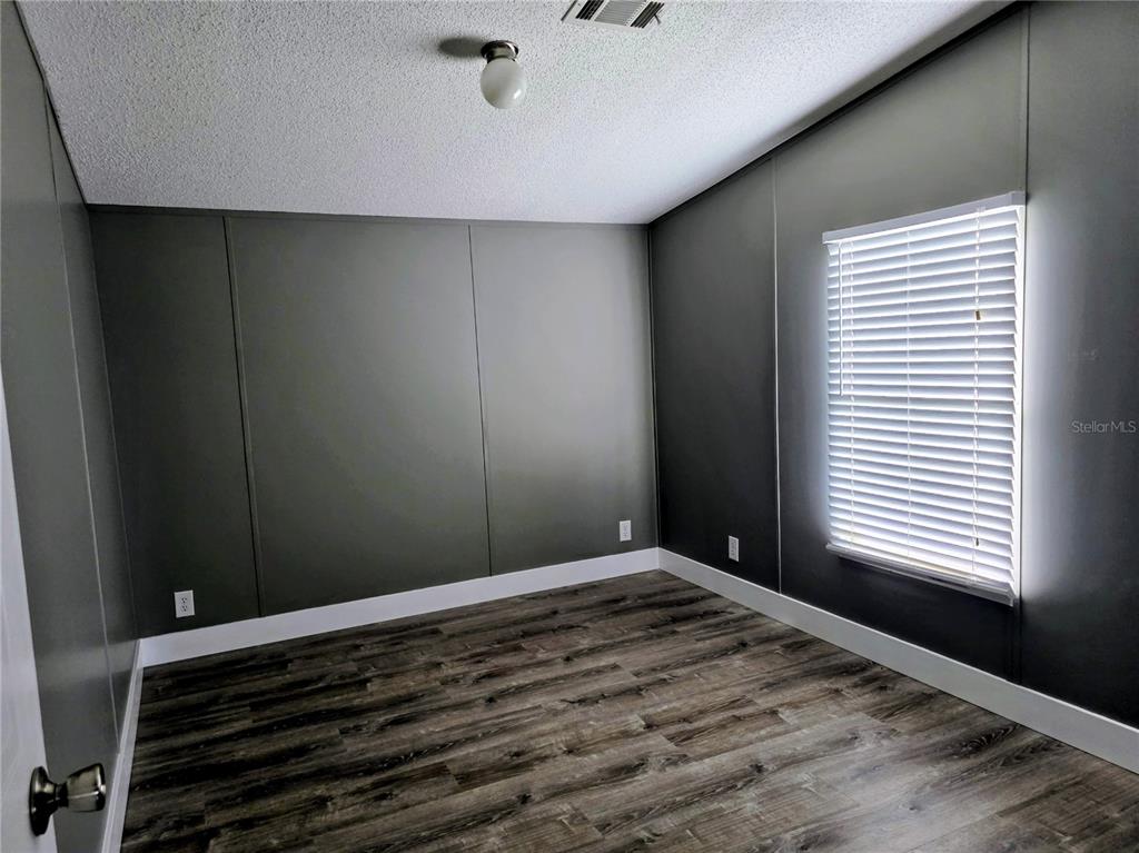 An empty bedroom features dark gray paneled walls, white trim, and wood-look flooring — 205 W SHELL POINT ROAD Bldg A, RUSKIN, FL
