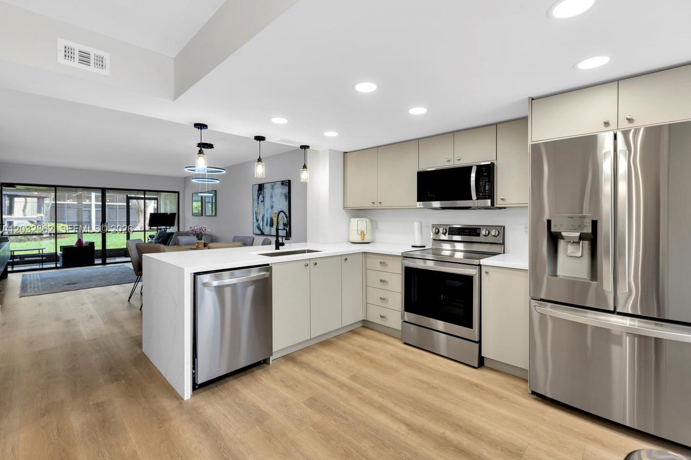 A modern kitchen features light-toned cabinetry, stainless steel appliances, and a white waterfall island countertop — 1929 SW 15th St # 39, Deerfield Beach FL 33442, DEERFIELD BEACH, FL