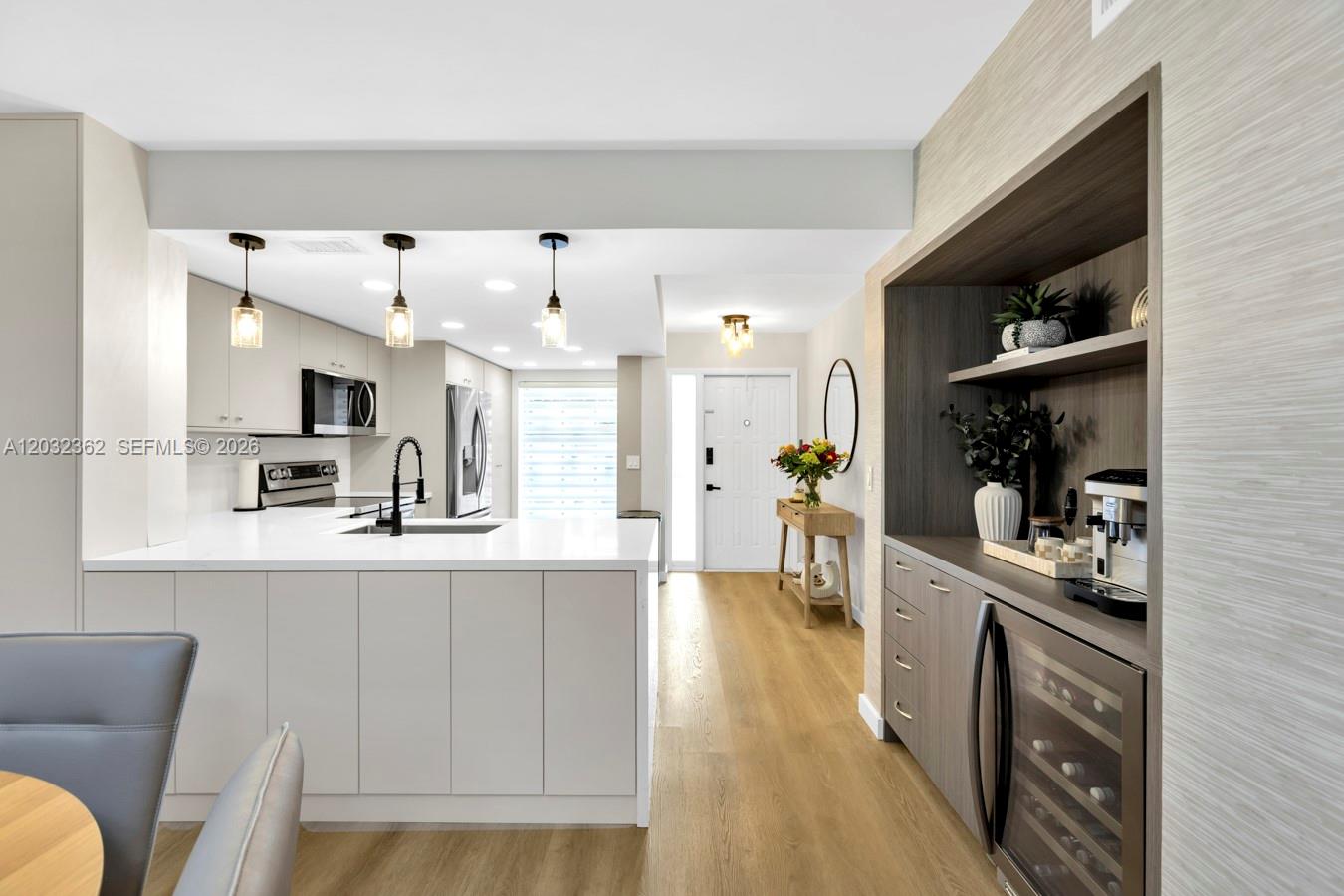 A modern kitchen features white cabinetry, a central island, and a built-in wood-toned coffee bar — 1929 SW 15th St # 39, Deerfield Beach FL 33442, DEERFIELD BEACH, FL