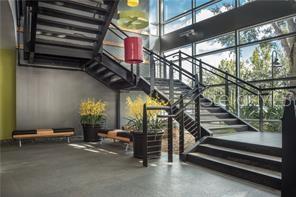 A modern building lobby features a black metal staircase, large windows, and potted yellow flowers — 429 S KELLER ROAD UNIT 310, ORLANDO, FL