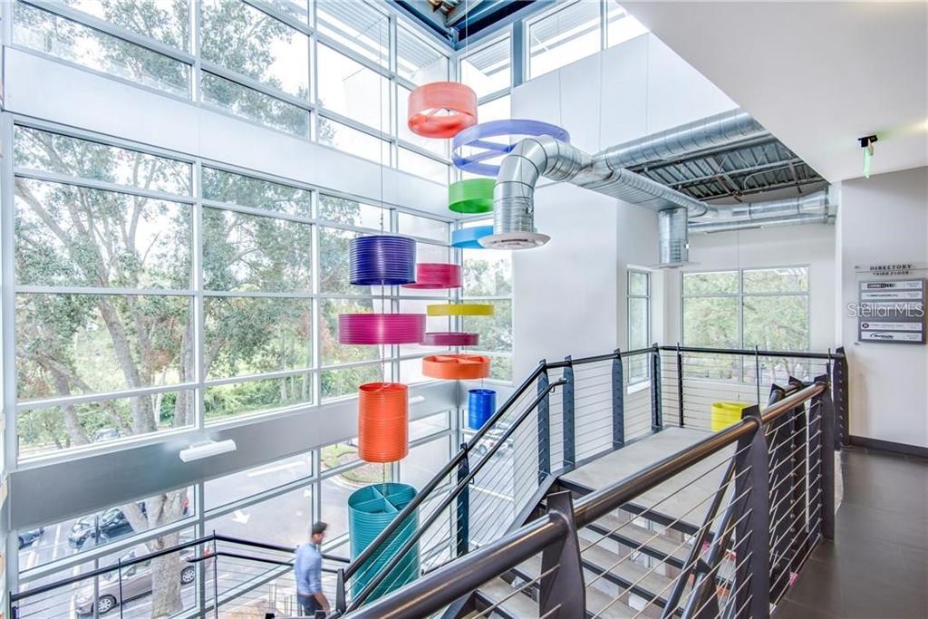 A modern office building interior features a multi-story staircase, large windows, and colorful hanging art — 429 S KELLER ROAD UNIT 310, ORLANDO, FL