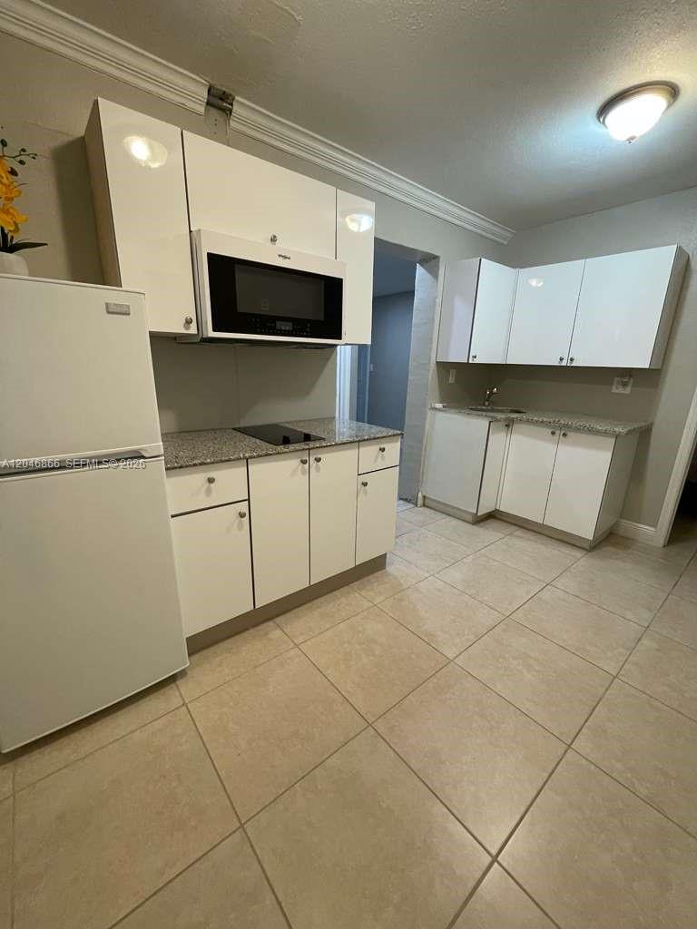 A kitchen features white cabinets, a microwave, a refrigerator, and light-colored tile flooring — 11730 SW 172nd St # 0, Miami FL 33177, MIAMI, FL