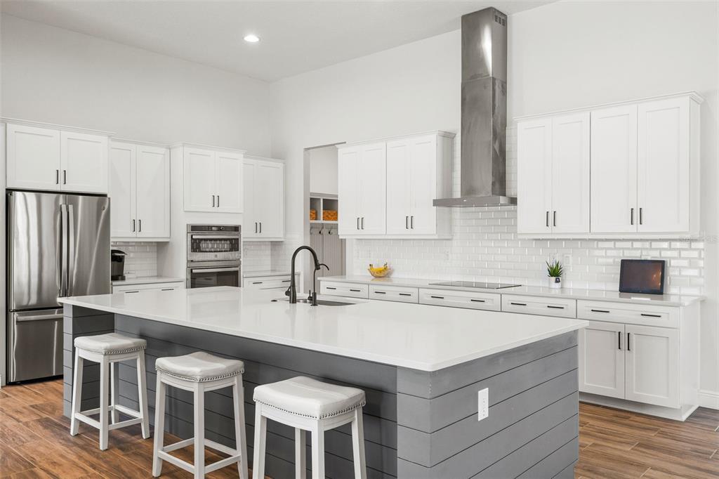 A modern kitchen features white cabinetry, a large gray island with seating, and stainless appliances — 34653 HEAVENLY LANE, DADE CITY, FL